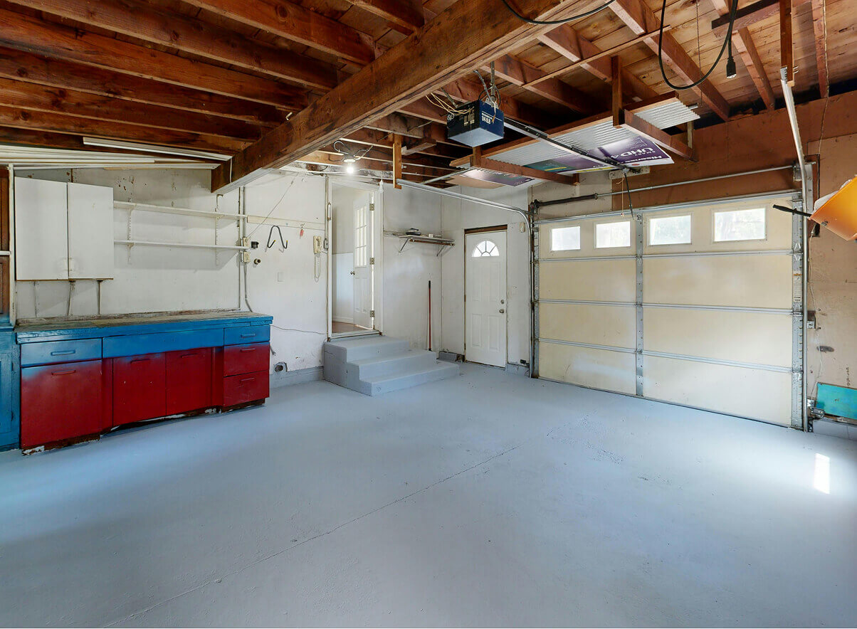 Resultaat van een professionele garageontruiming: een volledig lege en bezemschone garage met een grijze vloer en houten balkenplafond.