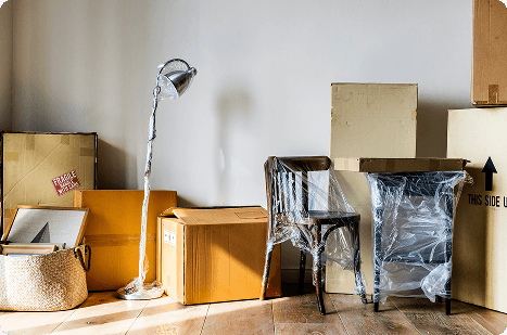 Een woonkamer vol ingepakte dozen en meubels in folie tijdens de voorbereiding van een woningontruiming.